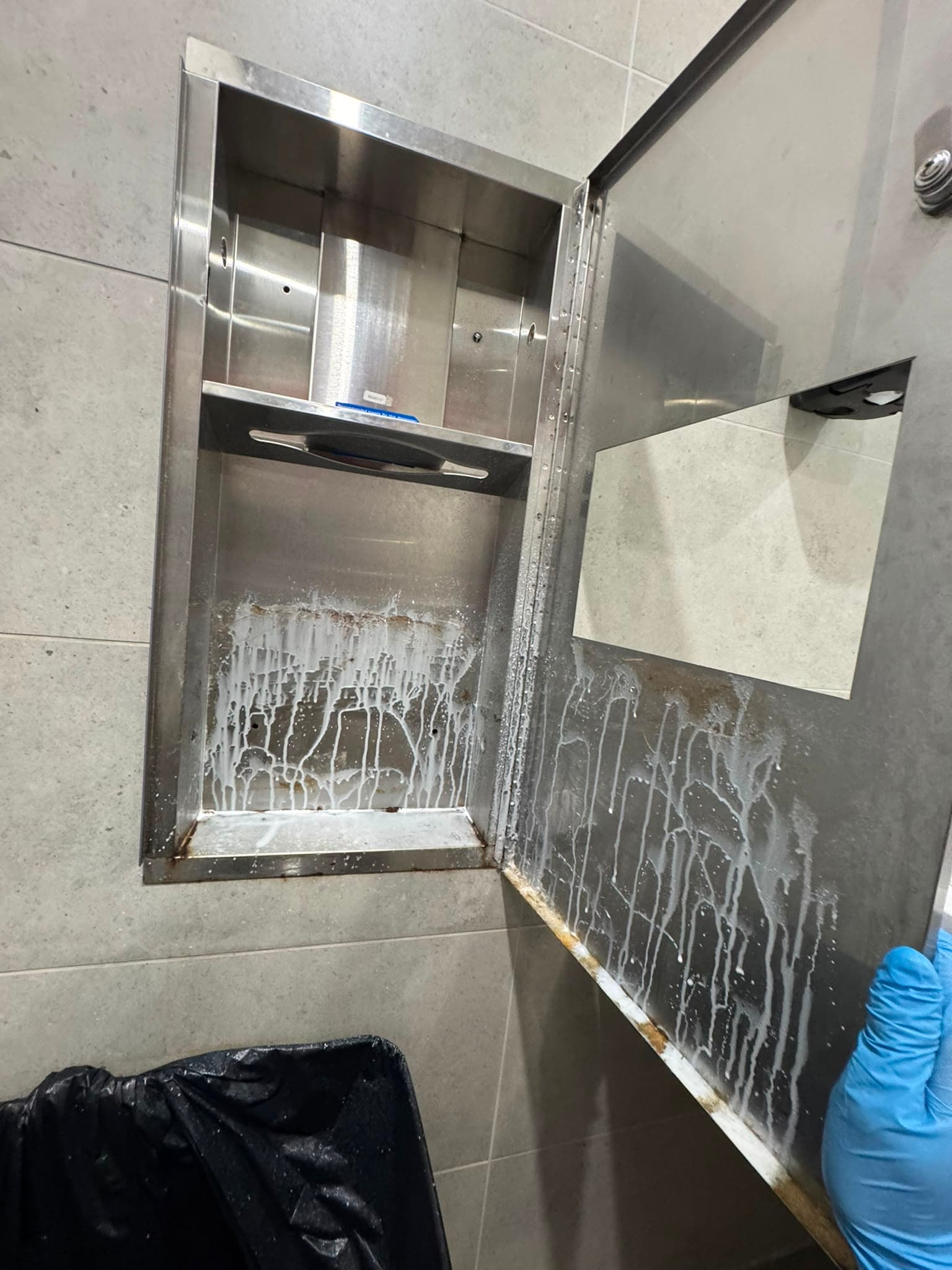 Grimy stainless washroom dispenser recess before cleaning